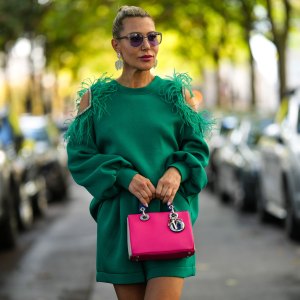 PARIS, FRANCE - OCTOBER 01: Olga Ferrara wears black circle sunglasses, silver rhinestones fringed earrings, a green cut-out shoulder / embroidered feather / embroidered rhinestones / belted short jumpsuit, a neon pink / beige / navy blue shiny leather handbag from Dior, outside Elie Saab, during Paris Fashion Week - Womenswear Spring/Summer 2023, on October 01, 2022 in Paris, France. (Photo by Edward Berthelot/Getty Images)