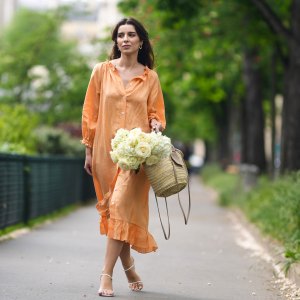 PARIS, FRANCE - MAY 10: Ketevan Giorgadze @katie.one wears gold earrings, a long buttoned coral loungewear linen The Sleeper dress with puffy sleeves, gold rings, a wicker with brown shiny leather detail Le Panier Soleil Jacquemus tote-bag, white strappy low heeled Raye sandals, on May 10, 2021 in Paris, France. (Photo by Edward Berthelot/Getty Images)