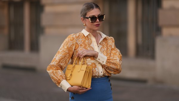 BERLIN, GERMANY - JUNE 07: Aline Kaplan is seen wearing large sunglasses with beige, brown and black pattern from Tibi; chunky golden hoop earrings; several golden necklaces; a creme-white blouse with floral orange pattern from Sézane; a blue high-waisted pair of trousers with two button borders on the hips from Sézane; golden rings and a yellow leather handbag from Saint Laurent on June 07, 2024 in Berlin, Germany. (Photo by Jeremy Moeller/Getty Images)