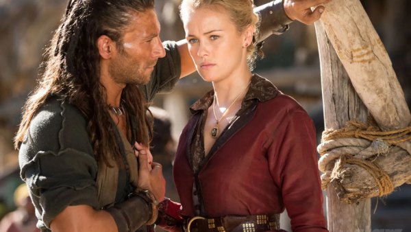 A pirate stands in front of a woman in Black Sails.