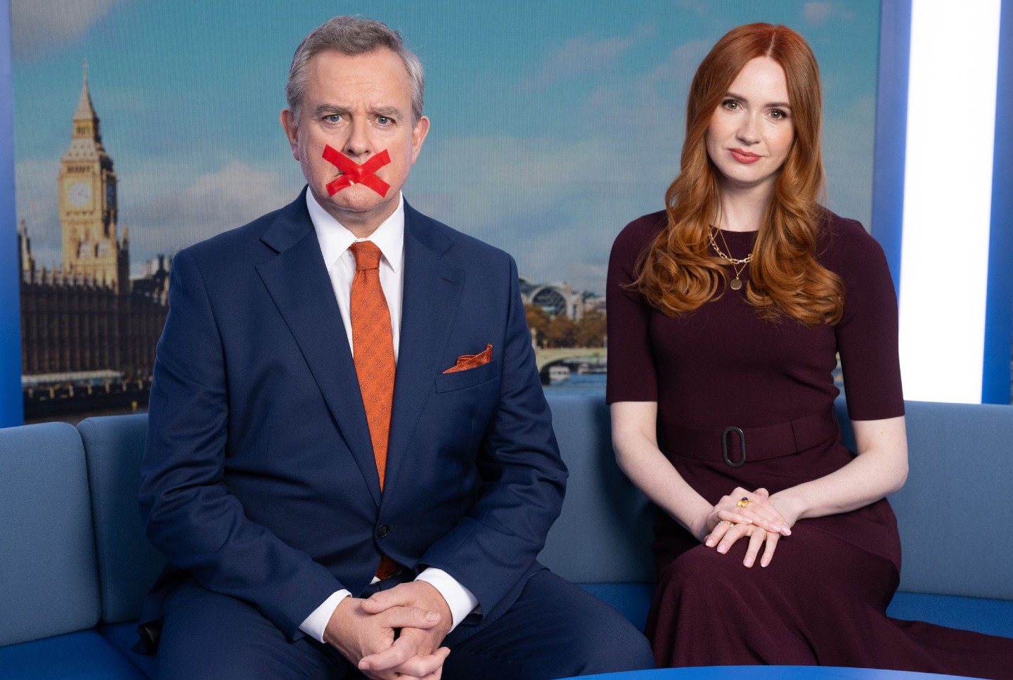 A man and a woman sit on a couch in Douglas Is Cancelled.