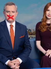 A man and a woman sit on a couch in Douglas Is Cancelled.