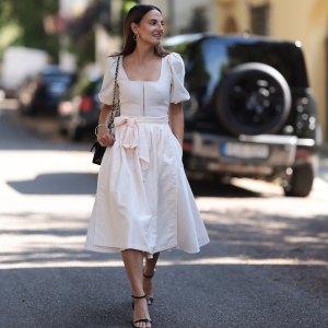 MUNICH, GERMANY - AUGUST 15: Anna Winter seen wearing silver hoop earrings, Cocovero creamy white dirndl / short dress, Chanel black leather bag, silver bangle and black leather heels, on August 15, 2024 in Munich, Germany. (Photo by Jeremy Moeller/Getty Images)