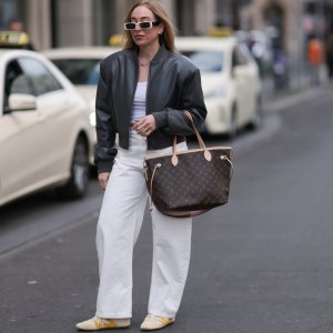 BERLIN, GERMANY - APRIL 09: Sonia Lyson seen wearing Linda Farrow bold white rectangular sunglasses that add a trendy touch, Zara white cotton fitted crop top, Zara high-waisted, wide-leg white relaxed jeans / denim pants, The Frankie Shop black, slightly glossy bomber jacket, Louis Vuitton brown Neverfull tote bag in the classic monogram print and Louis Vuitton beige Sneakerina sneakers / shoes with mustard yellow details, introducing a playful, sporty contrast to the otherwise minimalist outfit, on April 09, 2025 in Berlin, Germany. (Photo by Jeremy Moeller/Getty Images)