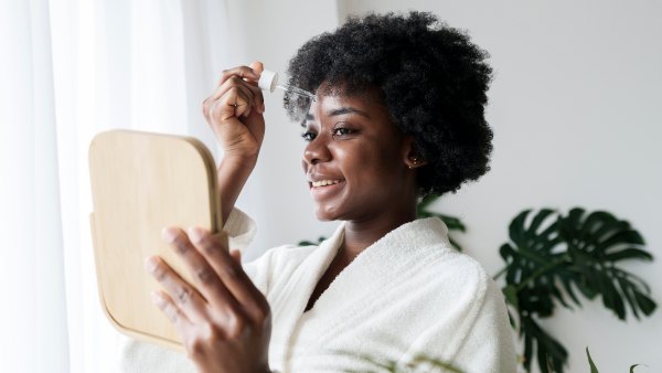 Happy young woman applying serum on face at home