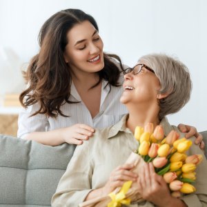 Beautiful young woman and her mother with flowers tulips in hands at home.