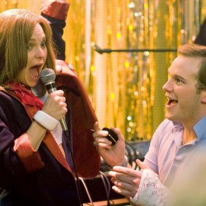 A guy looks at a girl singing in Take Me Home Tonight.