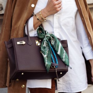 PARIS, FRANCE - MARCH 08: A guest wears white shirt, brown pants, brown suede jacket and brown Hermes bag with a green and white silk neck scarf outside the Hermes fashion show during the Womenswear Fall/Winter 2025/2026 as part of Paris Fashion Week on March 08, 2025 in Paris, France. (Photo by Raimonda Kulikauskiene/Getty Images)