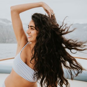 A beautiful young woman on a boat, runs her fingers through her long windswept hair - stock photo