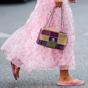 COPENHAGEN, DENMARK - AUGUST 10: A guest wears a white with pale pink flower print pattern / puffy shoulder / short sleeves / ruffled midi dress, a red bracelet, a yellow and purple shiny plastic checkered print pattern handbag from Chanel, pink flip flop , outside Baum und Pferdgarten, during Copenhagen Fashion Week Spring/Summer 2023, on August 10, 2022 in Copenhagen, Denmark. (Photo by Edward Berthelot/Getty Images)