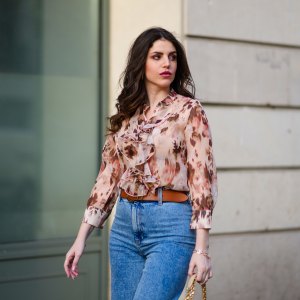 Sara Carnicella @lafillerebelle wears earrings from APM Monaco, a pink and purple floral print flowing shirt from Liu Jo, a brown leather belt from Mango, blue denim flared jeans from & Other Stories, on March 28, 2021 in Paris, France.