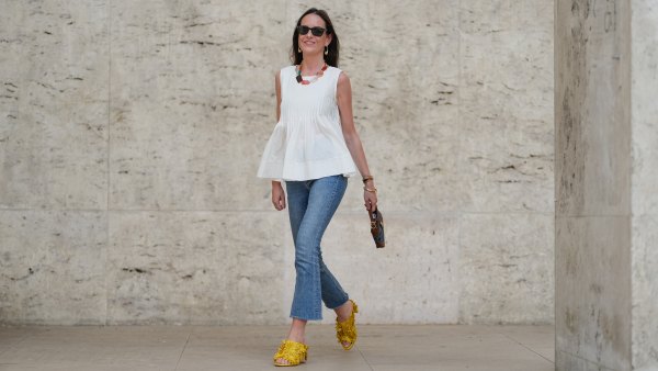Alba Garavito Torre wears black sunglasses, long straight brown hair with a center part, a white pleated peplum sleeveless blouse by Commense, and blue high-rise raw-hem denim jeans. A yellow clog sandal with floral detailing by AGL is worn, paired with a jean denim and brown mini Jackie handbag by Gucci. Accessories include a chunky necklace with colorful natural stones by Sempiterno Paris and gold jewelry. Full body shot, during a street style fashion photo session, on May 02, 2025 in Paris, France.
