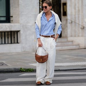 PARIS, FRANCE - APRIL 21: Diane Batoukina wears dark brown squared sunglasses from Dior, a pale blue cotton shirt from Ralph Lauren, a white matte large cashmere pullover from Weekend & Beyond, a brown braided leather belt from Ralph Lauren, white linen large pants from Ralph Lauren, a camel brown shiny leather crocodile print pattern handbag from Ralph Lauren, camel shiny leather with a gold metallic buckle loafers from Ralph Lauren, during a street style fashion photo session, on April 21, 2023 in Paris, France. (Photo by Edward Berthelot/Getty Images)