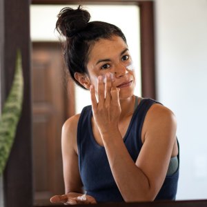 Woman applying white sunblock to face, looking at bathroom mirror - stock photo