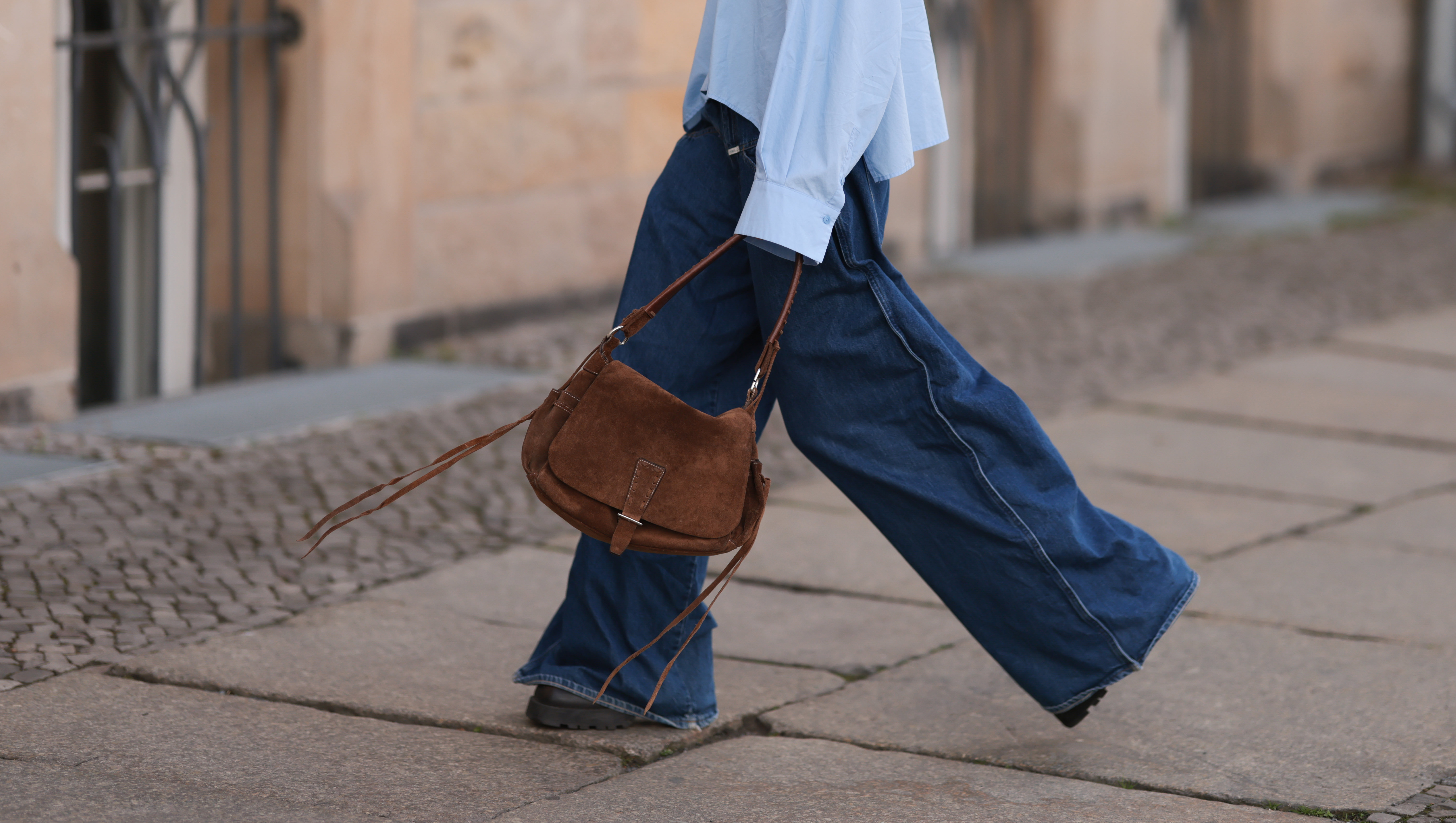 BERLIN, GERMANY - APRIL 22: Sophia Geiss is seen wearing two different-sized silver hoop earrings, oval brown glasses from Corlin, a silver nose ring, an oversized light blue shirt from Drykorn, wide-leg jeans with orange decorative seams from Closed, a brown vintage suede bag, and dark brown leather boots with chunky soles from Miista on April 22, 2025 in Berlin, Germany. (Photo by Jeremy Moeller/Getty Images)