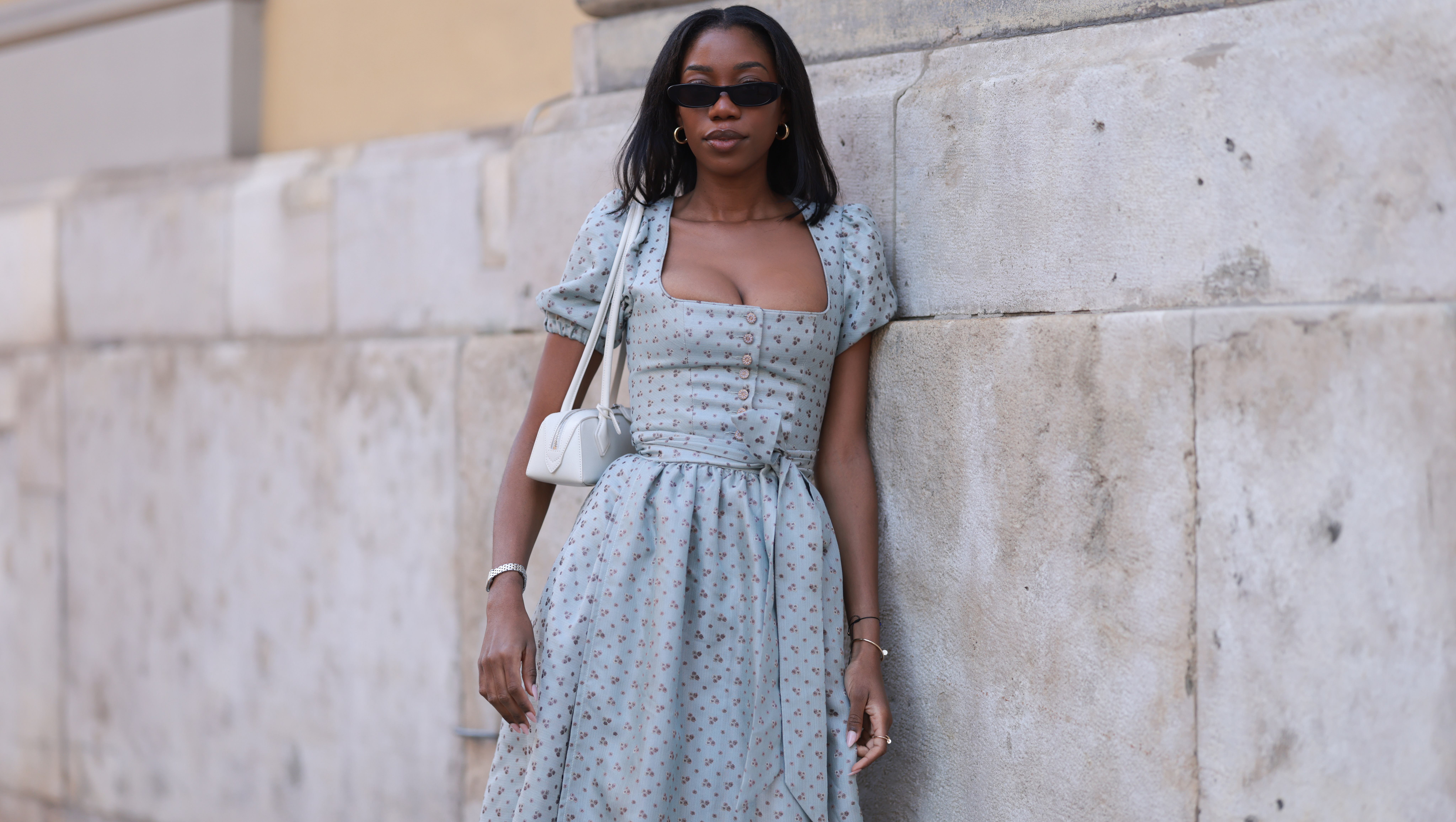 MUNICH, GERMANY - SEPTEMBER 21: Noutcha Lopes is seen wearing narrow rectangular sunglasses with a rounded black frame from Saint Laurent; chunky gold hoop earrings; a light blue dirndl with a flower pattern, a balconette neckline, a button placket, puffy short sleeves, and a bow from Limberry; a watch in silver and gold from Cartier; the yellow gold ‚ÄúJuste un Clou‚Äú bracelet and ring from Cartier; a black bracelet with a blue eye pendant; and a rectangular white leather ‚ÄúLe Teckle‚Äú bag with tubular handles from Ala√Øa during the opening day of the 2024 Munich Oktoberfest on September 21, 2024 in Munich, Germany. This year's Oktoberfest will run through October 6 and is expected to draw millions of visitors. (Photo by Jeremy Moeller/Getty Images)