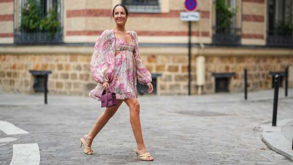 Alba Garavito Torre wears earrings, a pale pastel pink mini low-neck gathered and pleated floral print dress with puff shoulders / sleeves and ruffles, a purple Jacquemus bag, Bottega Veneta wicker sandals shoes, on August 04, 2021 in Paris, France.