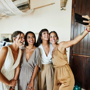 Medium wide shot of smiling and laughing bridesmaids tasking selfie in luxury hotel suite before wedding