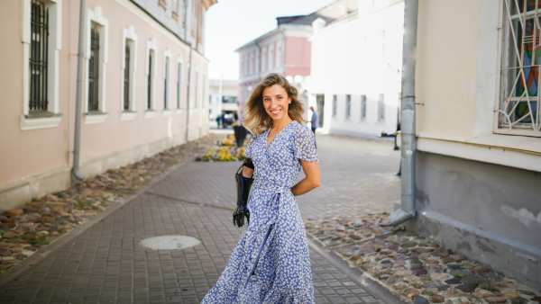 beautiful young slim woman in summer blue dress dance and walks through small town, local tourism