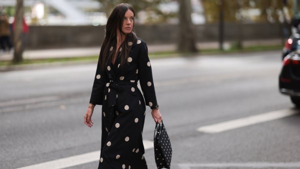 A Fashion Week guest is seen wearing round diamond stud earrings, a long-sleeved black midi dress with white polka dot pattern, notched lapels, and a tie belt; a gold bangle; a rose gold and black watch from Rolex; a gold ring; and a rectangular black handbag with a white polka dot pattern before the Elie Saab Womenswear Spring/Summer 2025 Show as part of Paris Fashion Week on September 28, 2024 in Paris, France.