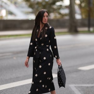 A Fashion Week guest is seen wearing round diamond stud earrings, a long-sleeved black midi dress with white polka dot pattern, notched lapels, and a tie belt; a gold bangle; a rose gold and black watch from Rolex; a gold ring; and a rectangular black handbag with a white polka dot pattern before the Elie Saab Womenswear Spring/Summer 2025 Show as part of Paris Fashion Week on September 28, 2024 in Paris, France.