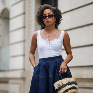 PARIS, FRANCE - MAY 08: Ellie Delphine wears sunglasses , golden earrings, a necklace, a white tank top, a blue midi denim gathered skirt, a beige and black striped fluffy bag, during a street style fashion photo session, on May 08, 2024 in Paris, France. (Photo by Edward Berthelot/Getty Images)