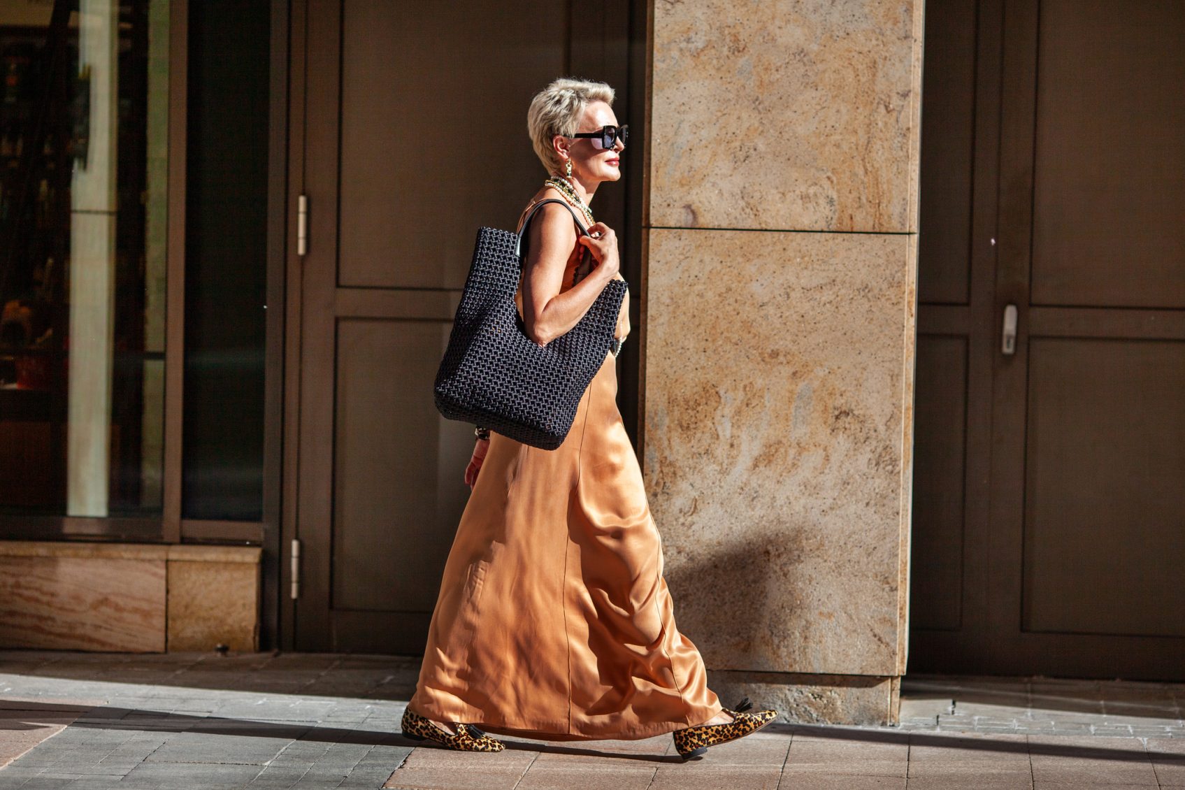 Stylish Mature Woman with Short Hairstyle Walks, Wearing Summer Beige maxi Dress and Large Handbag. Fashion Mode in City.
