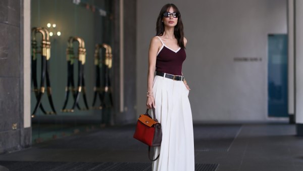 Heart Evangelista wears sunglasses from Dior, a burgundy low-neck tank top with white lines from Edition, a black leather belt, a white maxi long pleated skirt from Edition, golden bracelets, a brown / orange / red leather Kelly Hermes bag, Chanel shoes, during a street style fashion photo session, on November 15, 2023 in Singapore.