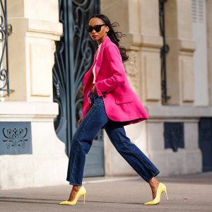 Emilie Joseph @in_fashionwetrust wears sunglasses, a bright neon pink oversized blazer jacket from Zara, a white crew neck crop top from H&M, high rise ribcage straight blue jeans in dark indigo from Levi's, a silk floral multicolor printed scarf worn as a belt from Kenzo, yellow high heels pointy stilettos shoes from Cosmoparis, on March 21, 2021 in Paris, France.