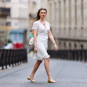 Fashion blogger @hippolyt.e wears a white lace with belted short ruffled dress from Nach Bijoux, rings and necklace from Nach Bijoux, a gold Chanel bracelet, a white matter leather shoulder bag from Charlie Paris, a silver and black Chanel watch, golden shoes, on May 20, 2021 in Paris, France.