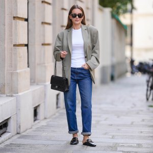 Diane Batoukina @diaanebt wears black sunglasses from Chanel, a white t-shirt, a beige gray oversized blazer jacket from Anine Bing, navy blue denim rolled-up large pants from Rouje, a black shiny grained leather Timeless handbag from Chanel, black shiny leather loafers mules from Massimo Dutti, during a street style fashion photo session, on April 15, 2022 in Paris, France.