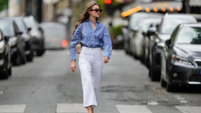 Segolene Hyppolite wears sunglasses, a blue and white oversized shirt from Tommy Hilfiger, a raffia beige bag from Vanessa Bruno, high waist white denim pants from Vanessa Bruno, Chanel slingback shoes in blue denim with black tips, during a street style fashion photo session, on May 20, 2024 in Paris, France.