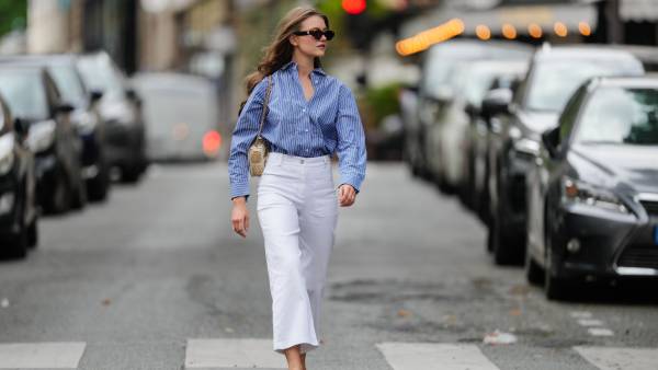 Segolene Hyppolite wears sunglasses, a blue and white oversized shirt from Tommy Hilfiger, a raffia beige bag from Vanessa Bruno, high waist white denim pants from Vanessa Bruno, Chanel slingback shoes in blue denim with black tips, during a street style fashion photo session, on May 20, 2024 in Paris, France.