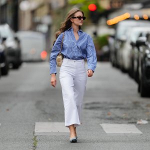 Segolene Hyppolite wears sunglasses, a blue and white oversized shirt from Tommy Hilfiger, a raffia beige bag from Vanessa Bruno, high waist white denim pants from Vanessa Bruno, Chanel slingback shoes in blue denim with black tips, during a street style fashion photo session, on May 20, 2024 in Paris, France.