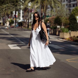 Gili Biegun wears a long white summer maxi dress, black bag with black and white scarf, silver necklaces, silver sea star earrings and black slippers with metal details during day five of the 78th Cannes Film Festival on May 17, 2025 in Cannes, France.