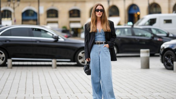 PARIS, FRANCE - SEPTEMBER 29: A guest wears black sunglasses, gold earrings, a blue denim embroidered seams heart-neck / corset top, a black oversized blazer jacket, a black shiny leather belt, blue denim large wide legs pants, black shiny leather handbag, black shiny leather ankle boots , outside Chloe, during Paris Fashion Week - Womenswear Spring/Summer 2023, on September 29, 2022 in Paris, France. (Photo by Edward Berthelot/Getty Images)