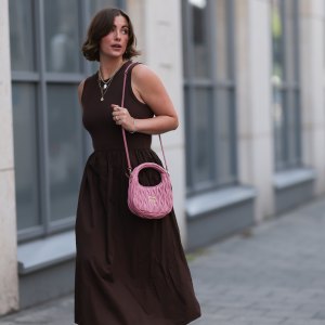 HAMBURG, GERMANY - JULY 18: Franzi Koenig is seen wearing several stud earrings, including gold seashell-shaped studs from fafe collection; layered gold necklaces with a seashell pendant, an F-letter pendant, and a white beaded necklace with a round organic-shaped pendant, also from fafe collection; a sleeveless dark brown midi dress with a ribbed top, high round neckline, and a gathered A-line skirt; a quilted pink leather “Wander” Hobo bag with gold logo hardware and a long thin shoulder strap from Miu Miu; several chunky gold rings, paired with delicate bracelets, both from fafe collection; and dark brown slip-on sandals with kitten heels on July 18, 2025 in Hamburg, Germany. (Photo by Jeremy Moeller/Getty Images)