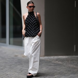 BERLIN, GERMANY - JUNE 04: Sophia Geiss is seen wearing silver hoop earrings in two different sizes; narrow oval black sunglasses from Saint Laurent; a silver nose ring; a flowy, backless halter-neck top in black with white polka dots from Zara; white wide-leg pants with a stretchy waistband and pocket details from The Room; a small rectangular black leather handbag with a gold YSL buckle from Yves Saint Laurent; a gold bangle; and black platform flip-flops from Zara on June 04, 2025 in Berlin, Germany. (Photo by Jeremy Moeller/Getty Images)