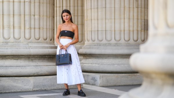 PARIS, FRANCE - JUNE 21: Alexandra Pereira wears silver and gold earrings, a black Prada shoulder-off crop-top, a white high accordion / gathered / pleated midi skirt with round holes from Prada, a black grained leather Galleria from Prada handbag, silver and diamonds rings, black shiny leather loafer shoes from Prada, on June 21, 2021 in Paris, France. (Photo by Edward Berthelot/Getty Images)