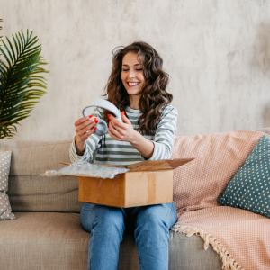 Beautiful mature woman unboxing a package with new headphones she ordered online at home.