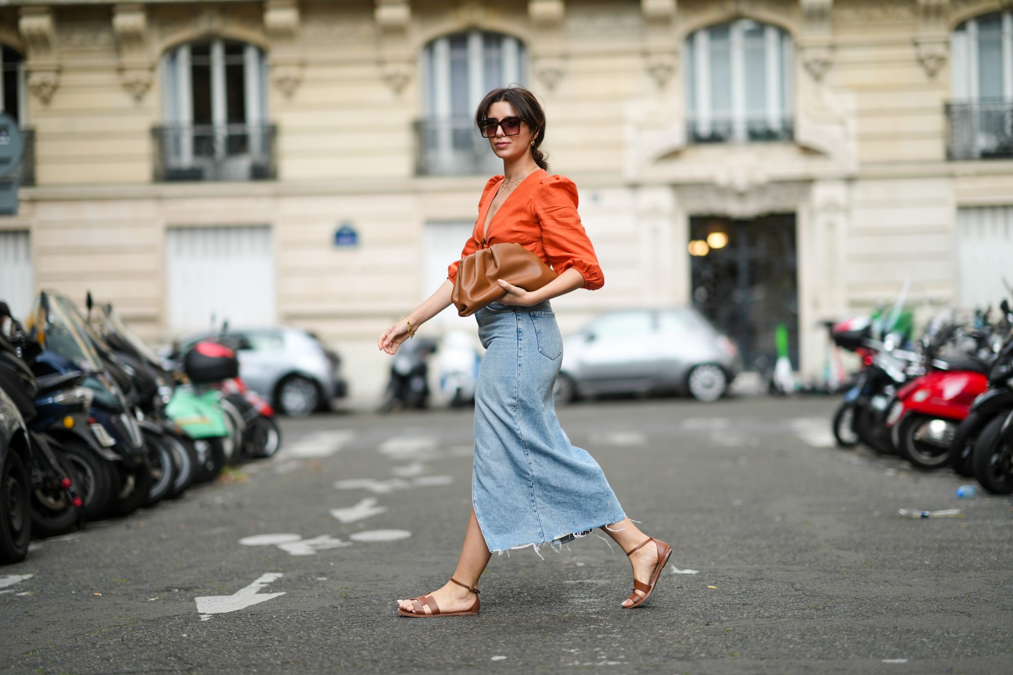 PARIS, FRANCE - AUGUST 28: Ketevan Giorgadze @katie.one wears black and gold chain sunglasses from Art's Sake, gold chain pendant necklaces, gold large earrings, an orange linen cropped / V-neck / puffy sleeves t-shirt from Kao, blue faded denim high waist ripped slit / split midi pencil skirt from Zara, a brown shiny ruffled leather Pouch handbag from Bottega Veneta, gold bracelets, brown shiny leather Santorini sandals from Hermes, on August 28, 2021 in Paris, France. (Photo by Edward Berthelot/Getty Images)