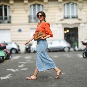 PARIS, FRANCE - AUGUST 28: Ketevan Giorgadze @katie.one wears black and gold chain sunglasses from Art's Sake, gold chain pendant necklaces, gold large earrings, an orange linen cropped / V-neck / puffy sleeves t-shirt from Kao, blue faded denim high waist ripped slit / split midi pencil skirt from Zara, a brown shiny ruffled leather Pouch handbag from Bottega Veneta, gold bracelets, brown shiny leather Santorini sandals from Hermes, on August 28, 2021 in Paris, France. (Photo by Edward Berthelot/Getty Images)