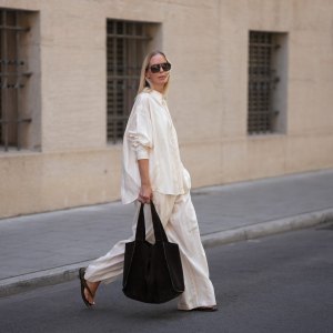 MUNICH, GERMANY - JUNE 18: Mirja Klein is seen wearing a matching set consisting of a white striped oversized dobby-weave shirt with collar and buttons down in the front from H&M and a white striped straight pull-on trousers with loose fit and straight legs from H&M; a black suede tote bag with slouchy design and open top from COS; black oversized aviator sunglasses from Tom Ford; a pair of khaki green suede flip flops from A.EMERY on June 18, 2025 in Munich, Germany. (Photo by Moritz Scholz/Getty Images)