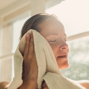 Woman toweling oneself off after bathing in sunny bathroom.