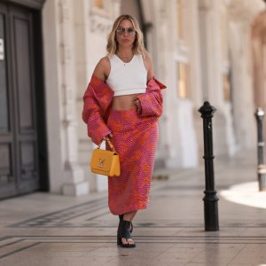 VIENNA, AUSTRIA - MAY 01: Karin Teigl wearing Baum & Pferdgarten matching cropped colorful shiny pink orange jacket and long midi skirt, Miu Miu black leather thong ankle boots, CYK white cropped bra top, Tom ford round gold glasses and Louis Vuitton yellow leather Twist bag on May 01, 2023 in Vienna, Austria. (Photo by Jeremy Moeller/Getty Images)
