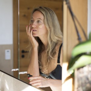 Woman applying makeup in front of bathroom mirror