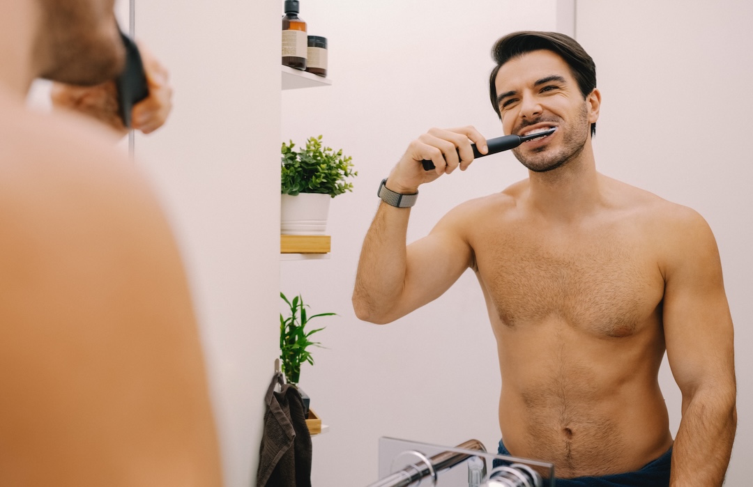 Мan in the bathroom is brushing his teeth with electric toothbrush