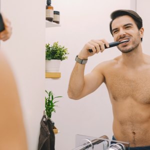Мan in the bathroom is brushing his teeth with electric toothbrush