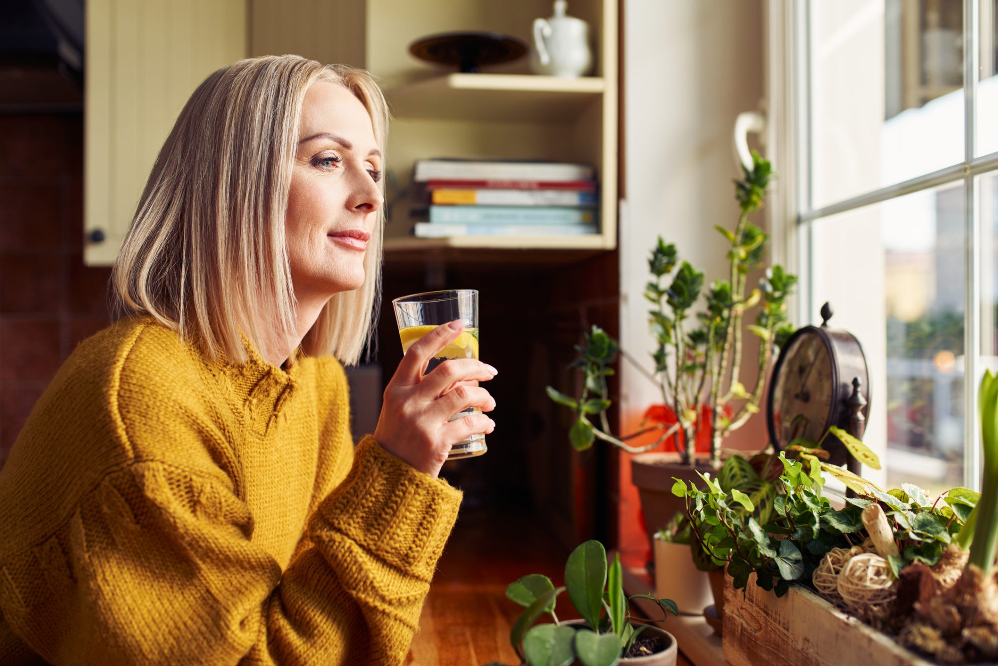 Mature woman drinking glass of water in the kitchen looking through the window