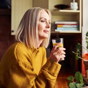 Mature woman drinking glass of water in the kitchen looking through the window